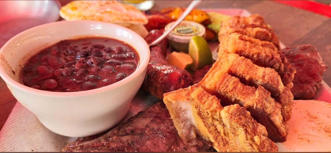 Platter with beans, fried pork, sausage, lime wedges, and grilled vegetables.