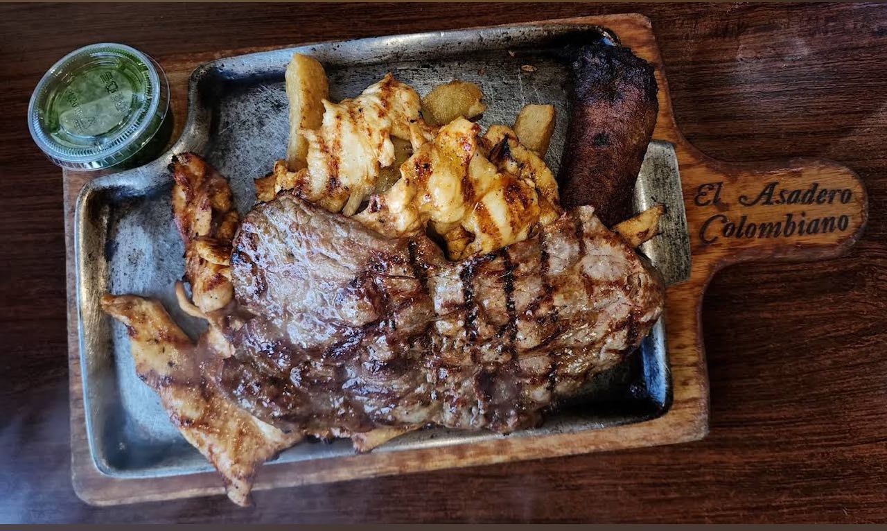 Grilled meat platter with fries and sauce on a wooden board labeled El Asadero Colombiano.